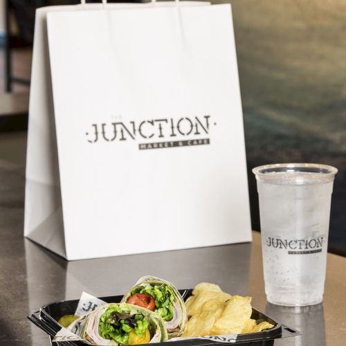 A takeout bag and cup from "Junction" beside a tray with wraps and chips are on a table.