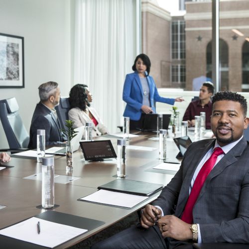 A group of professionals is sitting around a conference table, engaged in a meeting, with one person standing and speaking.
