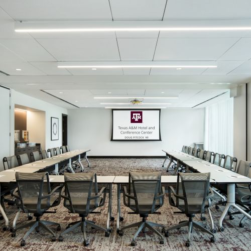 A conference room with U-shaped seating, chairs, carpeted floor, and a screen displaying "Texas A&M Hotel and Conference Center" is shown.