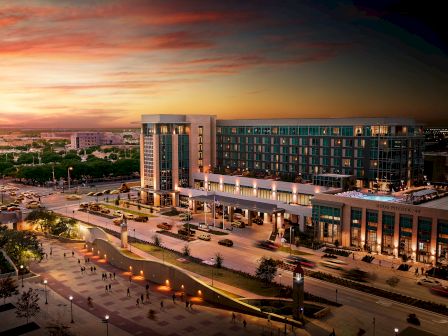 The image shows a modern building complex at dusk with busy streets and a vibrant sunset sky.
