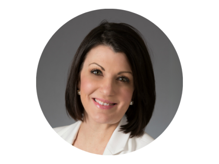 A person with short, dark hair, smiling, wearing a white jacket against a gray background in a circular frame.