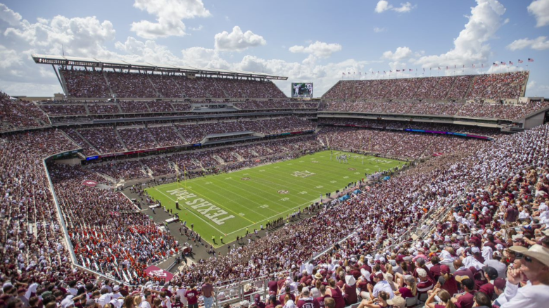 A football game in progress at a large, packed stadium under a blue sky with scattered clouds.