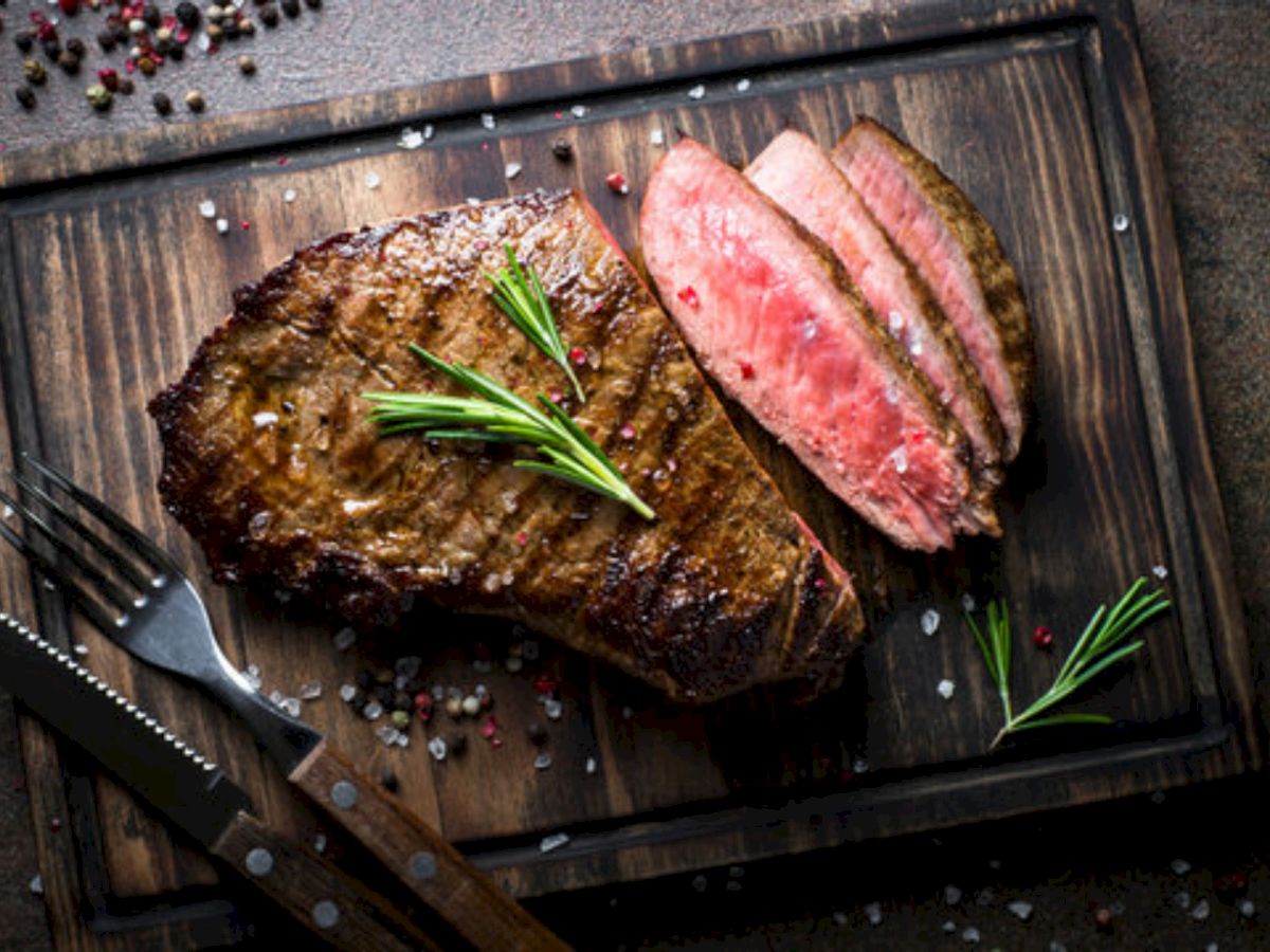 A juicy herb-crusted steak, sliced pink in the center, resting on a dark cutting board with rosemary sprigs and coarse salt for garnish.