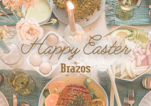 A festive Easter setting with floral decor, eggs, candle, drinks, and dishes including roasted meat. Text reads "Happy Easter" and "Brazos".