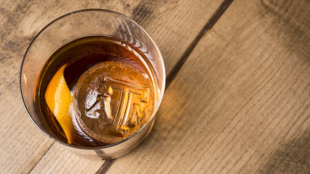 A glass of whiskey with ice and an orange slice on a wooden table, viewed from above.
