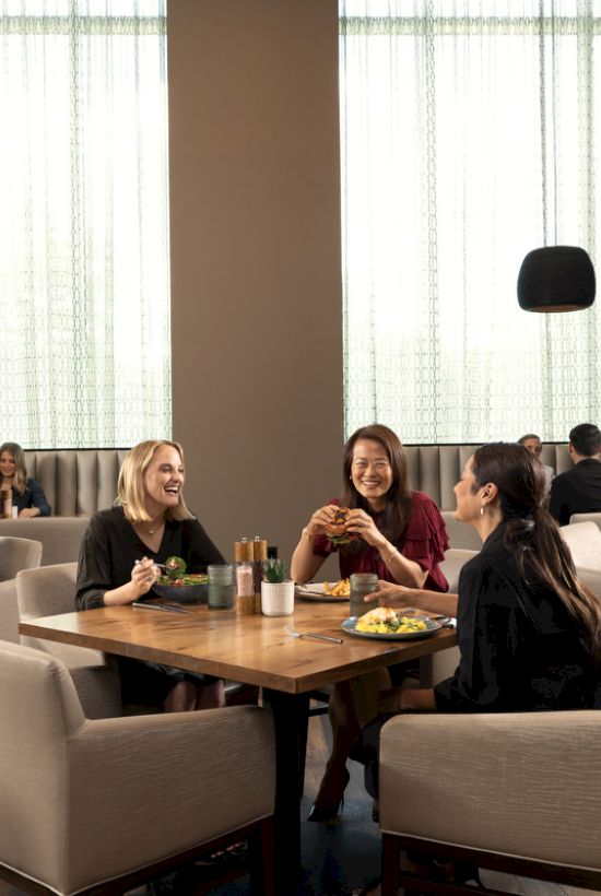 A group of people sitting at tables in a modern dining area, enjoying food and conversation, with artwork and soft lighting around them.