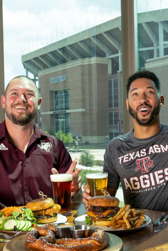 Two people are enjoying food and drinks in a restaurant with a view of a stadium in the background.
