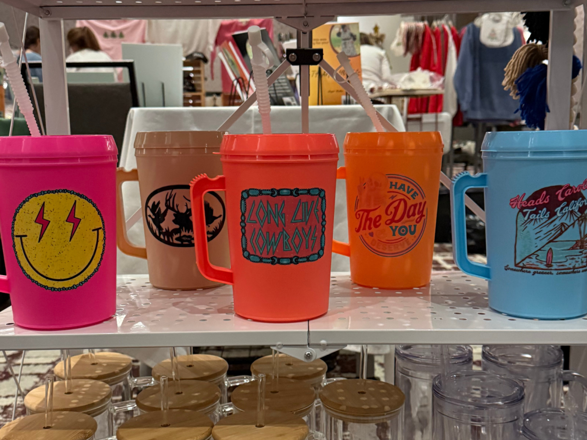 A shelf displays colorful mugs with various designs and slogans, some with straws.
