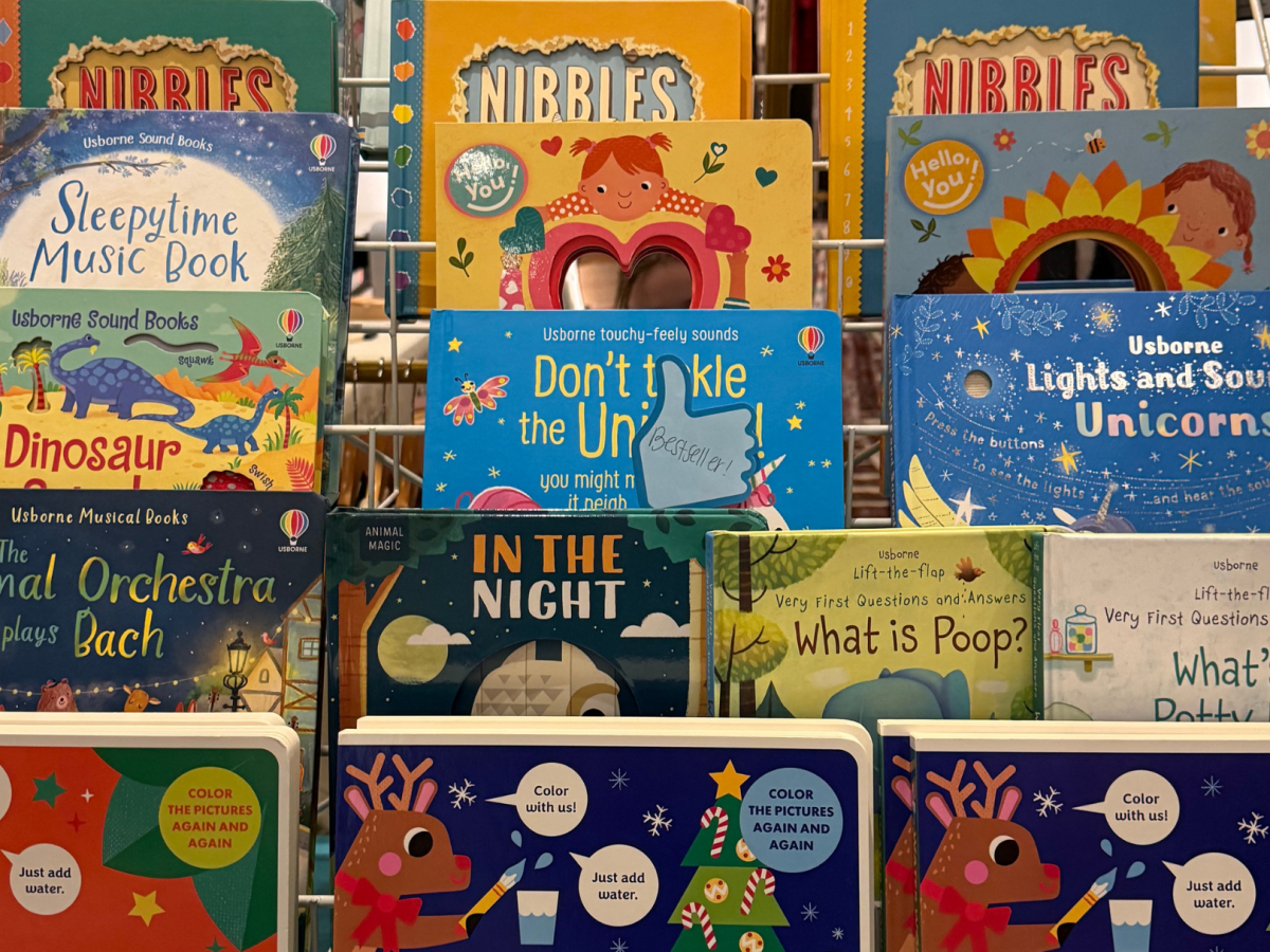 The image shows a display of children's books with colorful covers, featuring titles about dinosaurs, unicorns, music, and more.