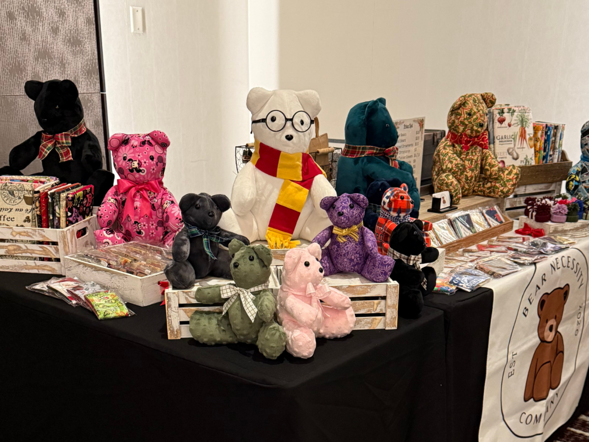 A display table featuring colorful teddy bears, assorted products, and treats is set up at a market or event.