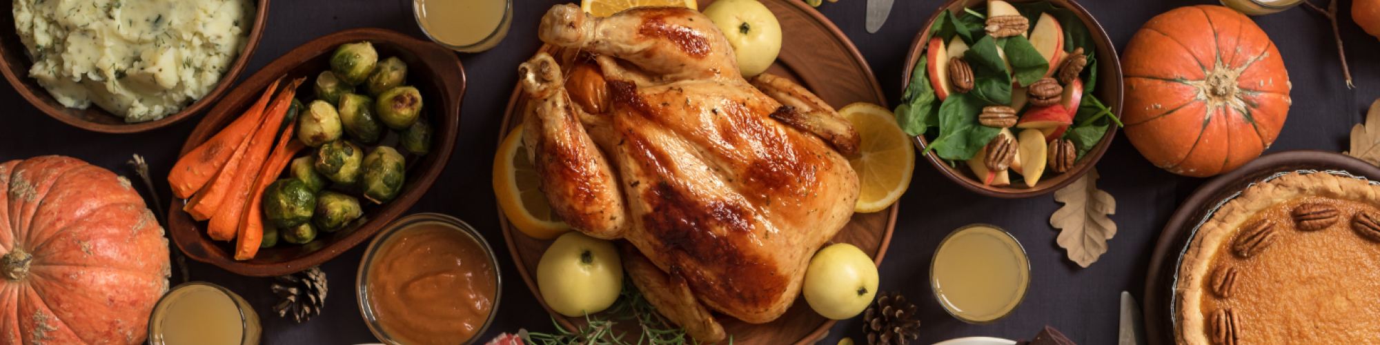 A festive table with roast turkey, mashed potatoes, vegetables, pie, and autumn decor, perfect for a holiday meal setting.