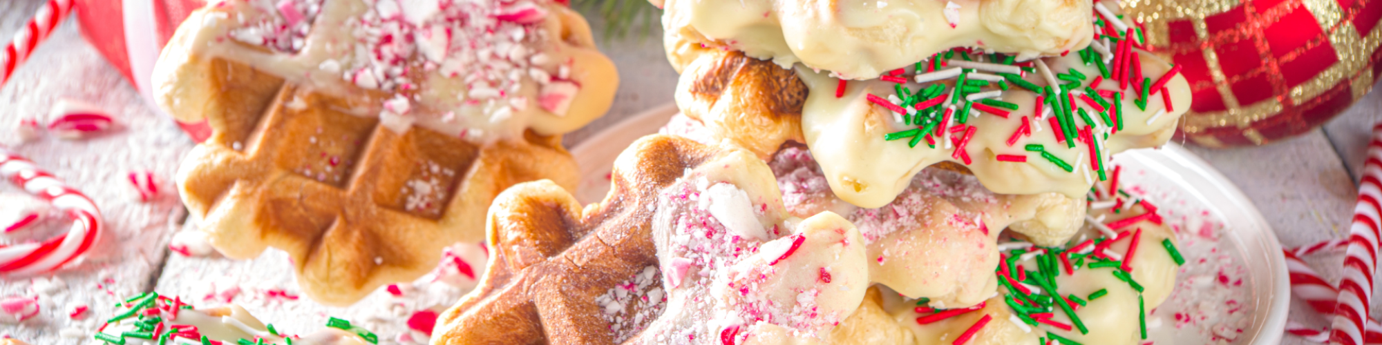 Festive waffles topped with white chocolate, crushed candy canes, and sprinkles, surrounded by holiday decorations and gifts.