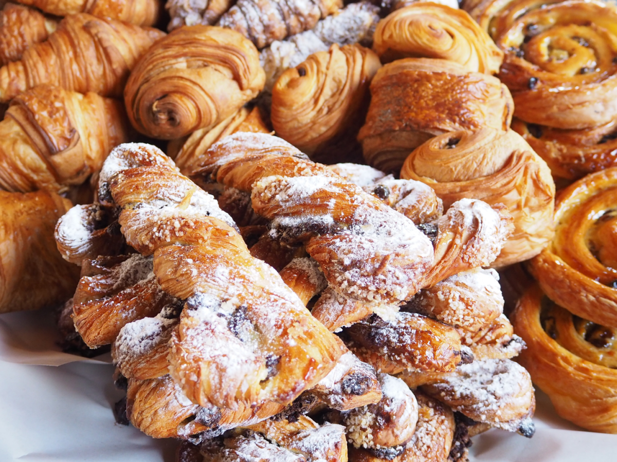 A variety of pastries, including croissants and spiral rolls, dusted with powdered sugar, are displayed on a tray.