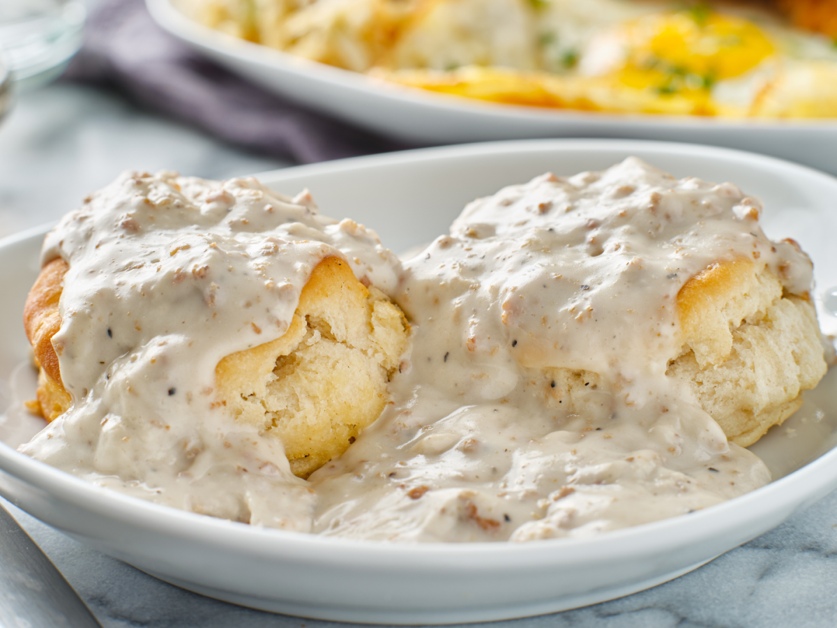 Biscuits smothered in gravy, served on a white plate, with a knife on the table.