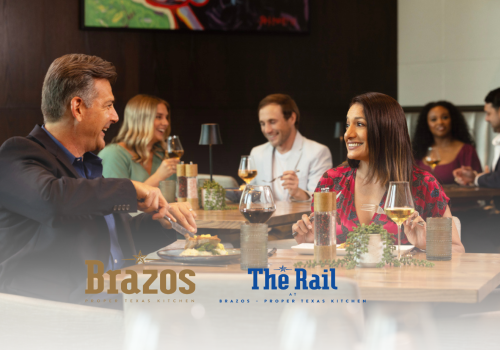 People dining and socializing at a restaurant, two visible logos: Brazos and The Rail. Everyone is smiling and engaged in conversation.