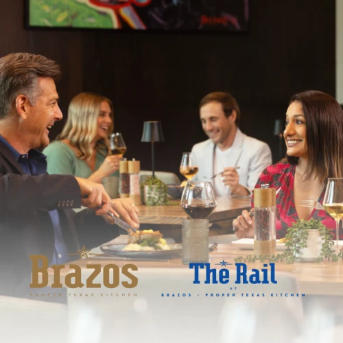 People dining and socializing at a restaurant, two visible logos: Brazos and The Rail. Everyone is smiling and engaged in conversation.