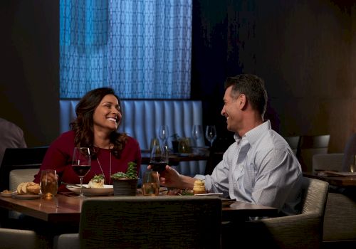Two people enjoy a warm dinner date, laughing and chatting across a table with drinks and dessert in a cozy, softly lit restaurant.