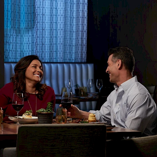 Two people enjoy a warm dinner date, laughing and chatting across a table with drinks and dessert in a cozy, softly lit restaurant.