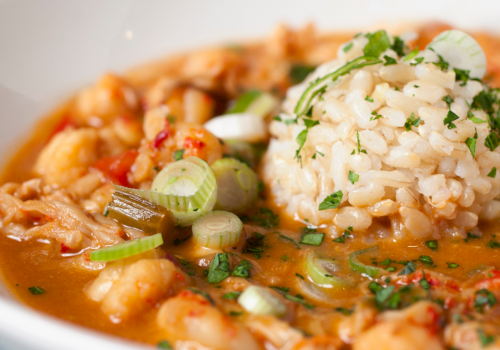 A steaming bowl of shrimp gumbo with rice, seafood, and herbs, in a savory tomato-based broth.