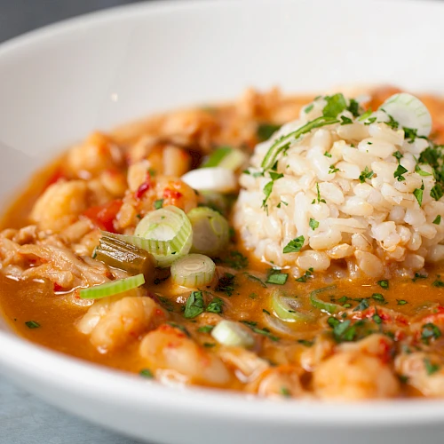 A steaming bowl of shrimp gumbo with rice, seafood, and herbs, in a savory tomato-based broth.